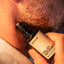 Close-up of stubbled lower face with Beardbrand Old Money Eau de Parfum roll-on bottle held against the skin.