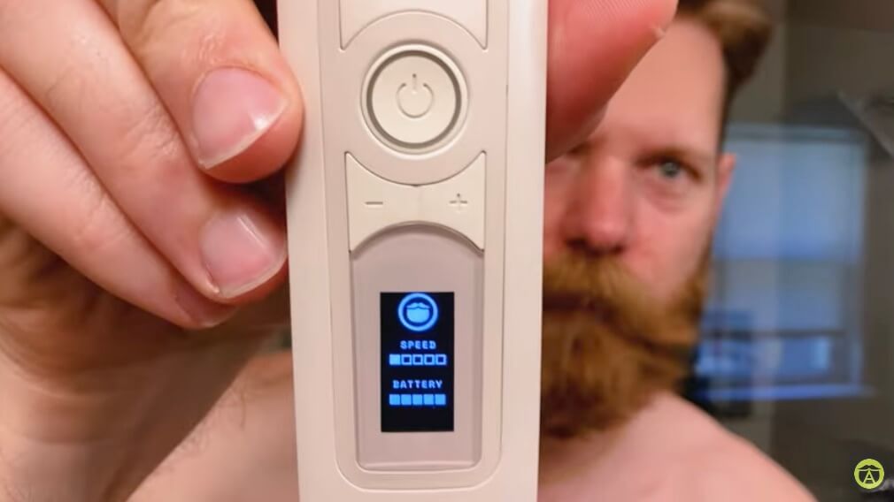 Eric Bandholz, Founder of Beardbrand, holding up the new Utility Trimmer close to the camera. The trimmer's display shows the current speed setting and battery level, with Eric's face slightly blurred in the background.