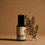 Desert Road Eau de Parfum bottle by Beardbrand set against a warm sand-colored background with a desert plant branch beside it. Image evokes a dry, rugged fragrance with notes of petrol, desert shrubs, leather, and baked earth.