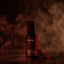 Four Vices Eau de Parfum bottle by Beardbrand surrounded by swirling smoke and coffee beans on a dark red background. Image evokes a rich, smoky fragrance with notes of coffee, tobacco, spice, and agarwood.