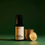 Beardbrand Old Money eau de parfum bottle beside stacked gold coins on a green background symbolizing the fragrance’s classic refined character.